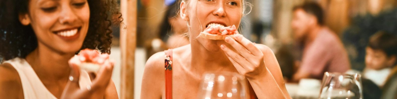 Two women enjoying bruschetta and wine at a vibrant outdoor restaurant.