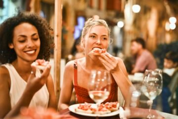 Two women enjoying bruschetta and wine at a vibrant outdoor restaurant.