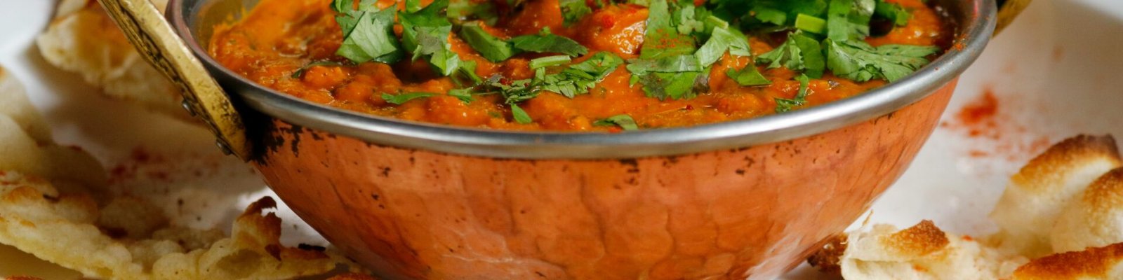 Delicious Indian curry garnished with cilantro served with naan in a copper dish.