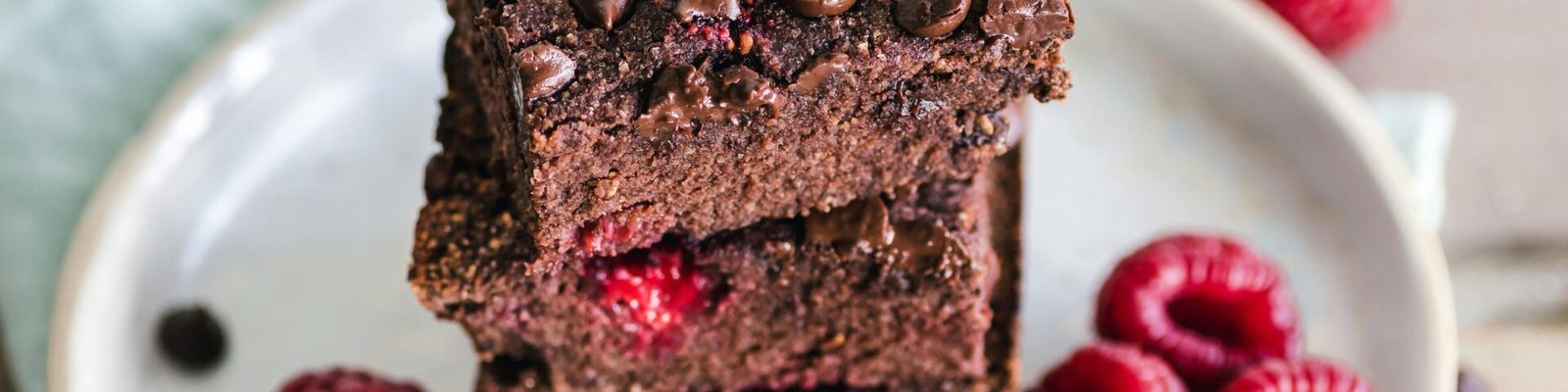 Close-up of deliciously indulgent chocolate raspberry brownies stacked on a ceramic plate with fresh raspberries.