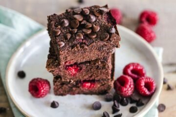 Close-up of deliciously indulgent chocolate raspberry brownies stacked on a ceramic plate with fresh raspberries.