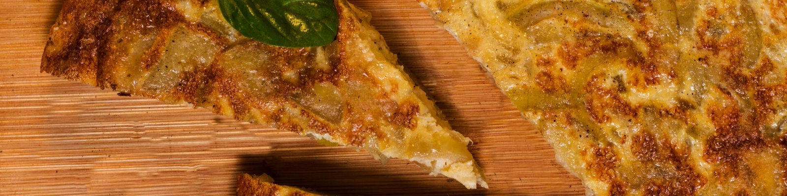 Close-up of traditional Spanish tortilla slices on a wooden board, garnished with basil.