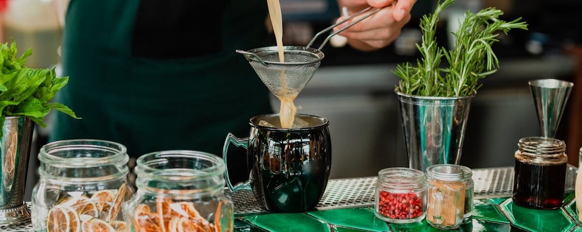 Bartender straining herbal cocktail in a chic bar setting, highlighting fresh ingredients.