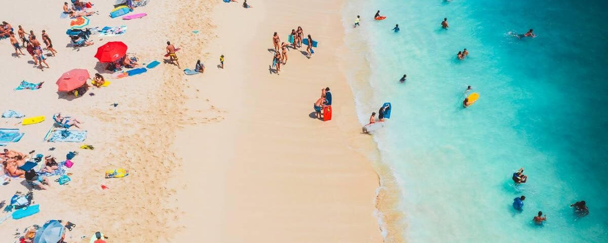Aerial photo captures tourists enjoying a sunny day on a vibrant beach with blue water.