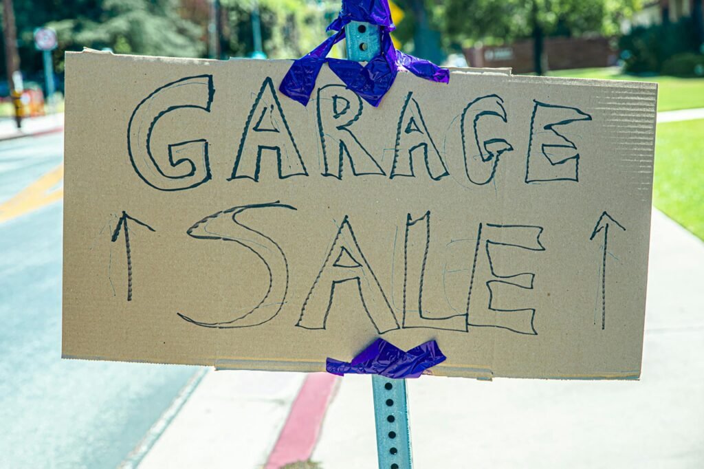 A handwritten garage sale sign taped on cardboard, displayed outdoors.