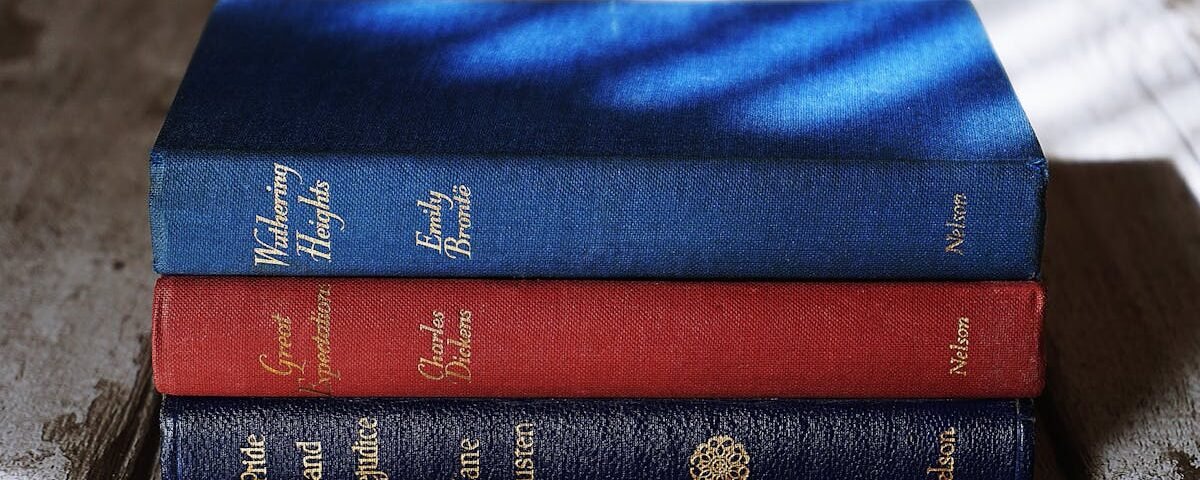 Stacked classics by Brontë, Dickens, and Austen on a wooden surface with dramatic lighting.
