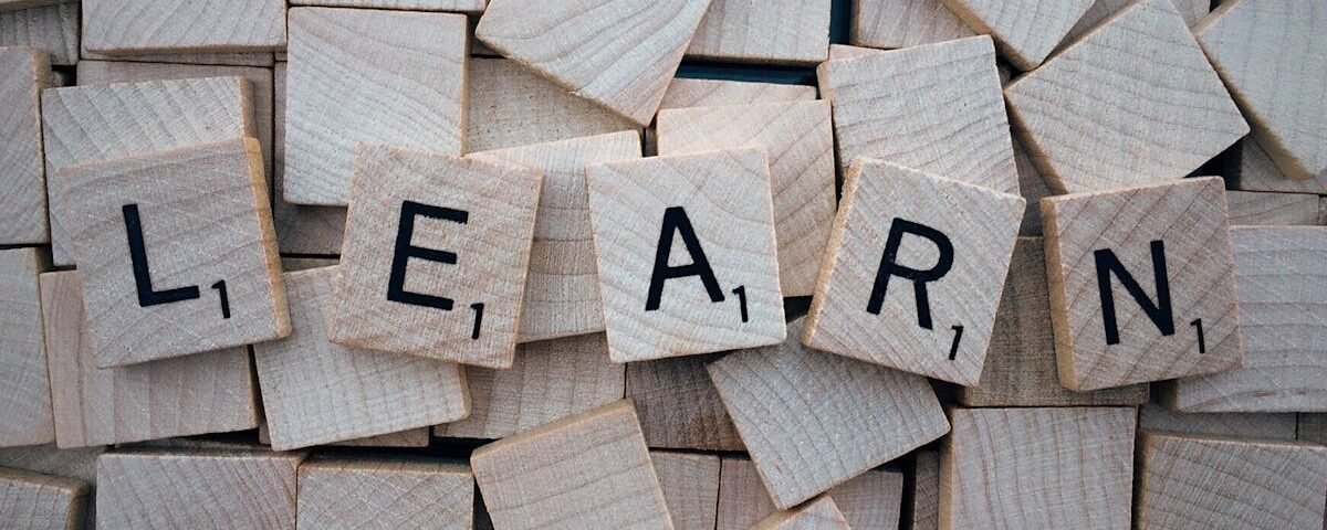 Wooden letter tiles arranged to spell 'learn' on a background of scattered tiles.