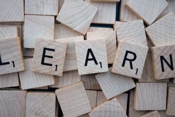 Wooden letter tiles arranged to spell 'learn' on a background of scattered tiles.