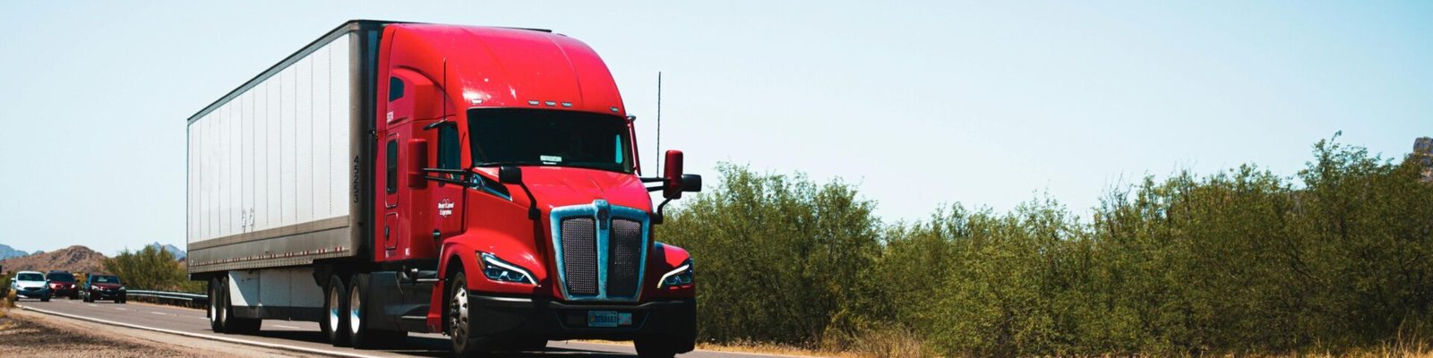 Vibrant red semi-trailer truck driving on an open highway under a clear blue sky.