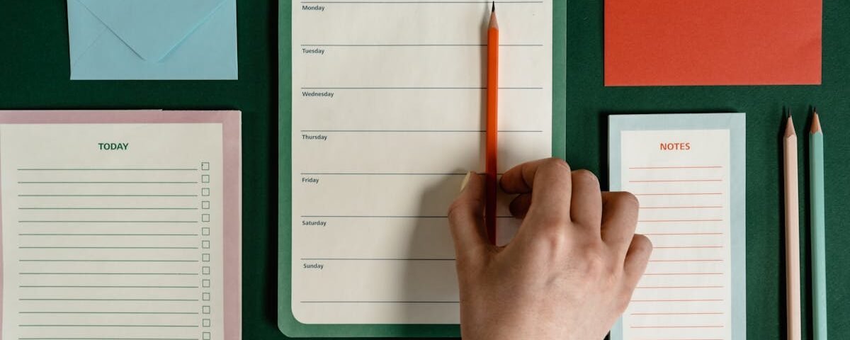Flat lay of stationery items including planners, envelopes, and pencils on a green surface.