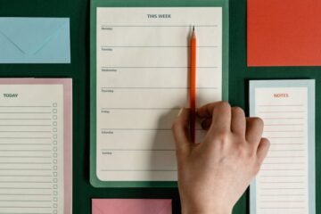 Flat lay of stationery items including planners, envelopes, and pencils on a green surface.