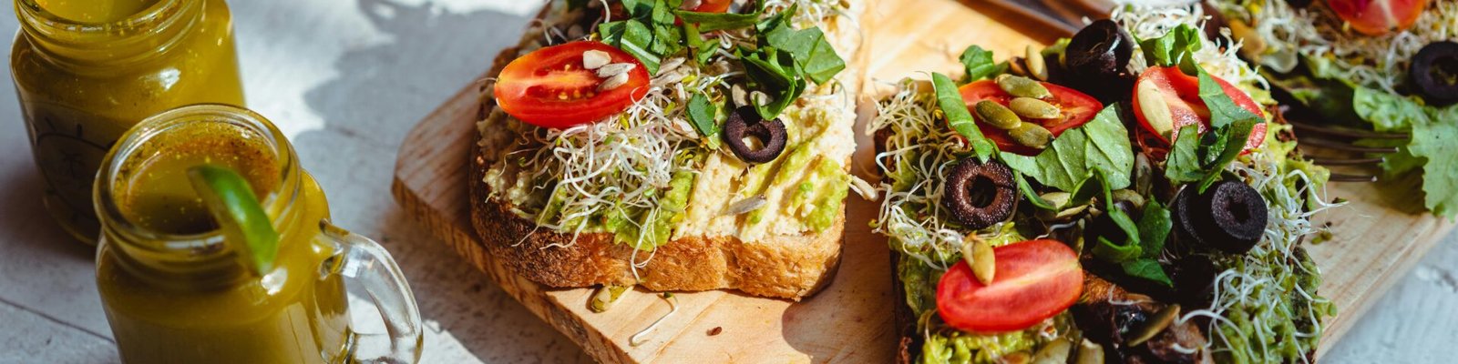 Close-up of fresh avocado toast with toppings, served with juices on a wooden board.