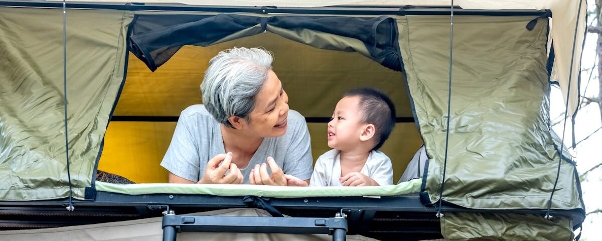 A senior and child enjoying outdoor rooftop tent camping, sharing smiles.