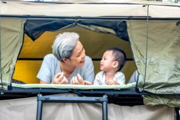 A senior and child enjoying outdoor rooftop tent camping, sharing smiles.
