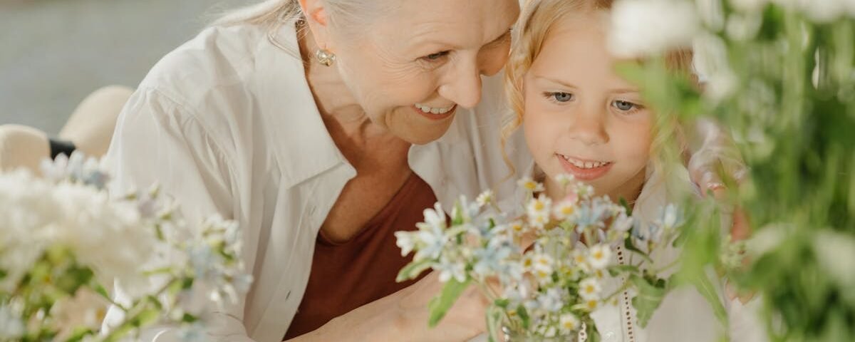 Grandmother and grandchild enjoying flowers at a table, sharing a joyful moment together indoors.