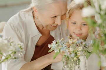 Grandmother and grandchild enjoying flowers at a table, sharing a joyful moment together indoors.