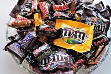 A bowl filled with various chocolate candies, including Twix, Snickers, and M&Ms, creating a vibrant dessert spread.