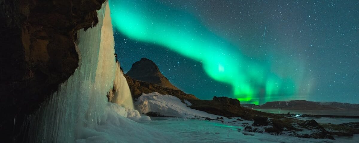 Stunning view of the Northern Lights over Kirkjufell mountain and frozen waterfall in Iceland. Perfect for nature lovers.