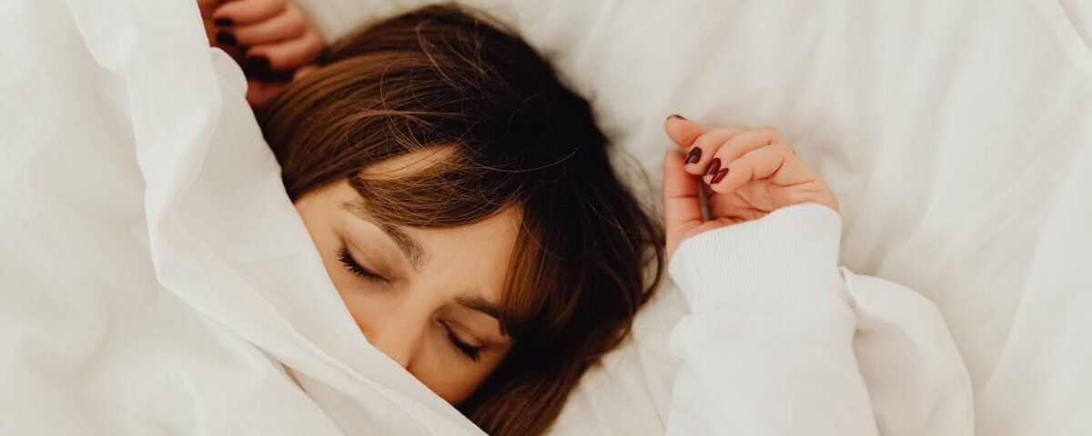 A woman peacefully sleeping under a white blanket in a cozy bed setting.