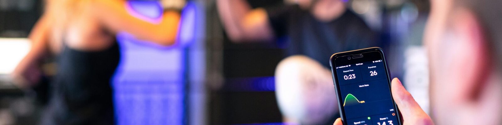 A woman boxing with a trainer while a fitness app tracks performance on a smartphone.