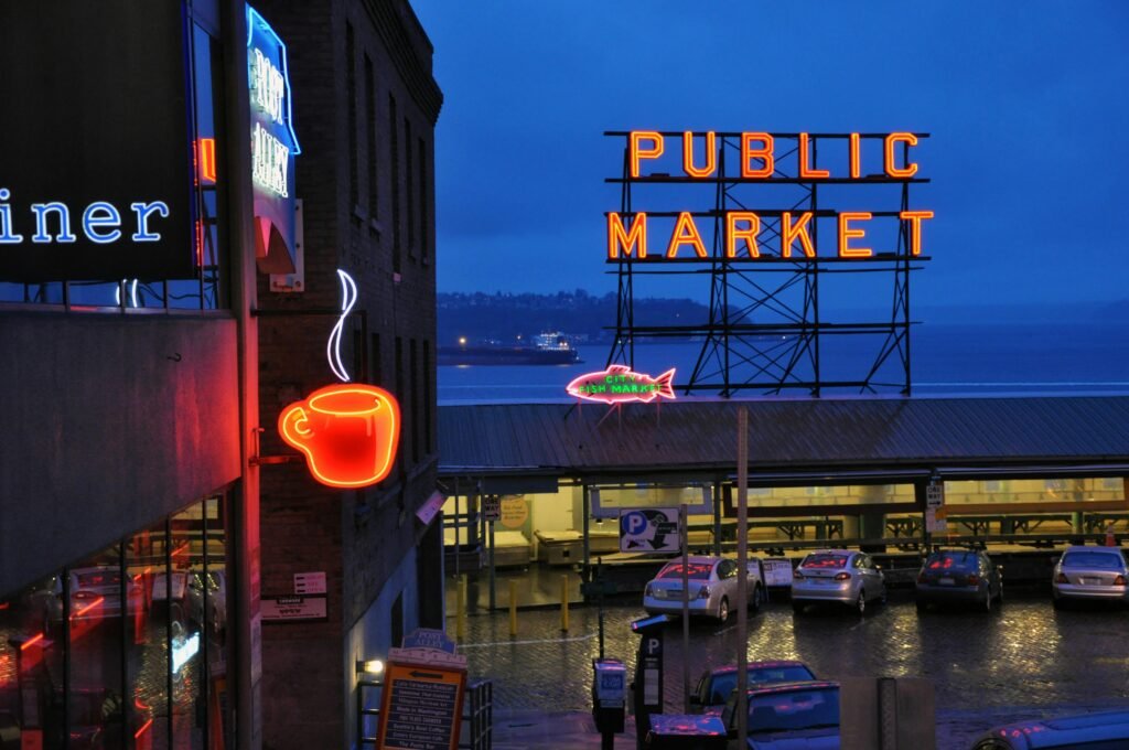 Vibrant nighttime view of Seattle's Public Market with neon coffee and market signs illuminated.
