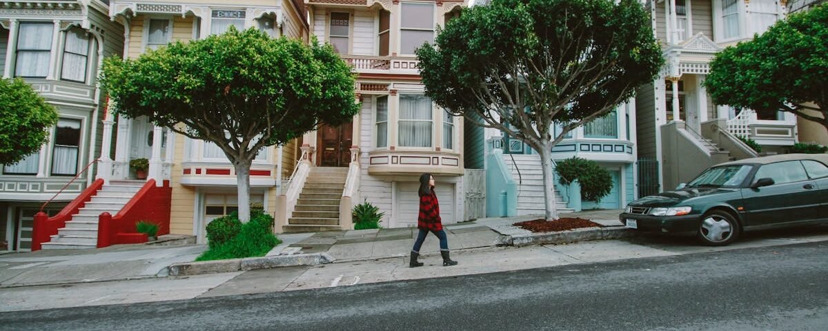 A woman walks past iconic Victorian houses in San Francisco, showcasing urban charm.