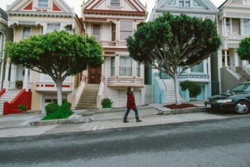 A woman walks past iconic Victorian houses in San Francisco, showcasing urban charm.
